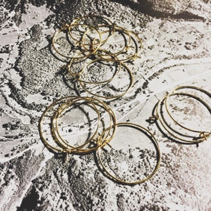 May include: A group of gold hoop earrings on a textured white surface. The hoops are various sizes and are stacked on top of each other.