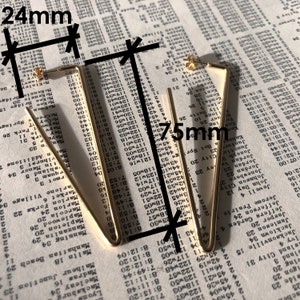 May include: A pair of gold-toned triangle-shaped hoop earrings. The earrings measure 24 mm in length and 75 mm in width.