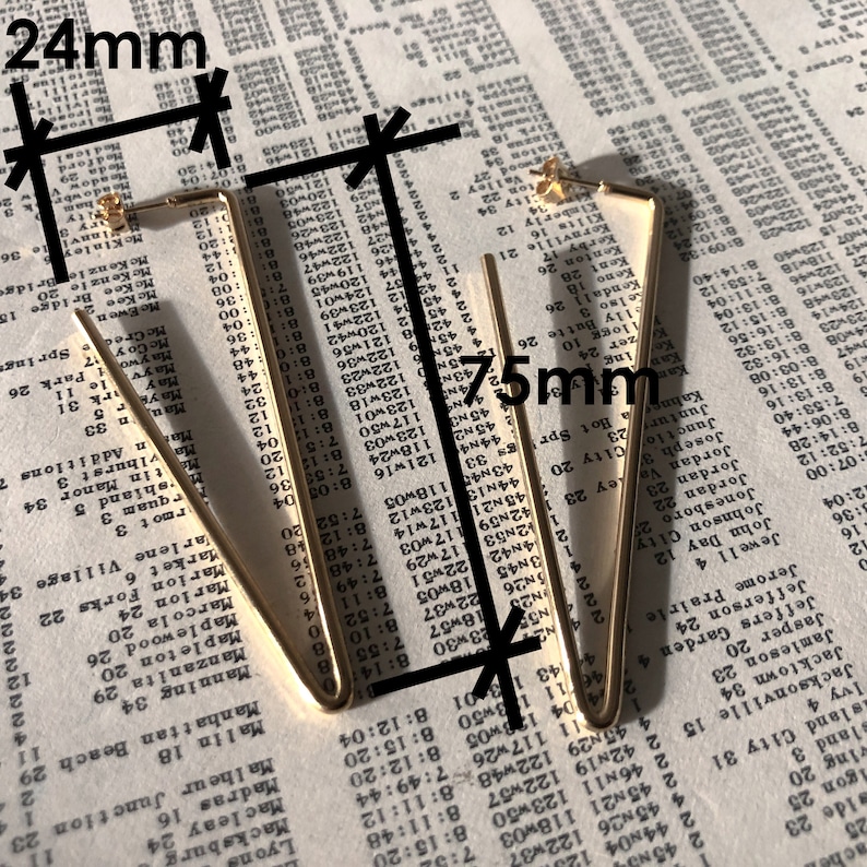 May include: A pair of gold-toned triangle-shaped hoop earrings. The earrings measure 24 mm in length and 75 mm in width.
