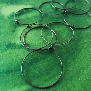 May include: A set of six silver hoop earrings of varying sizes, arranged on a green background.