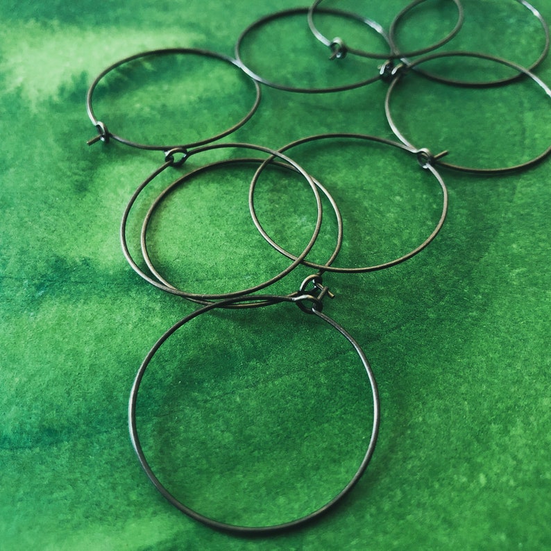 May include: A set of six silver hoop earrings of varying sizes, arranged on a green background.