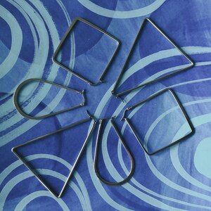 May include: Five silver hoop earrings of different shapes and sizes on a blue and white patterned background.