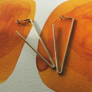 May include: A pair of gold-toned geometric earrings with a triangular shape.