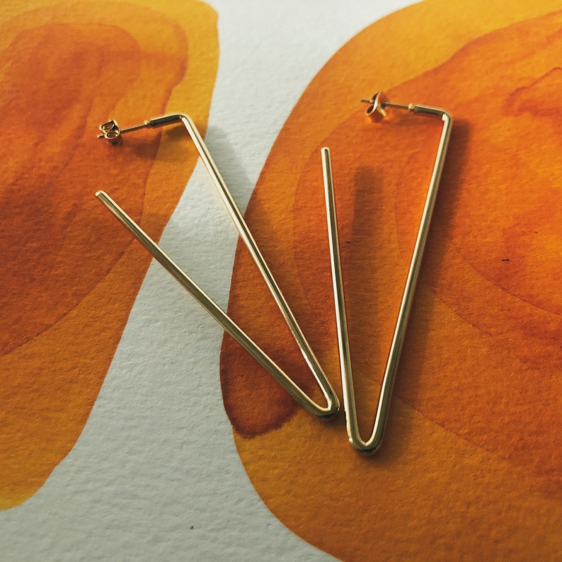 May include: A pair of gold-toned geometric earrings with a triangular shape.