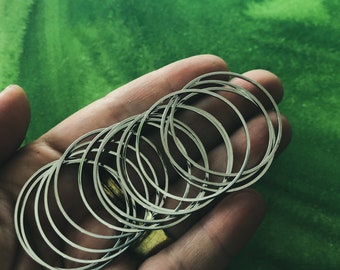 May include: A stack of silver bangles, arranged in a circle, held in a hand against a green background.