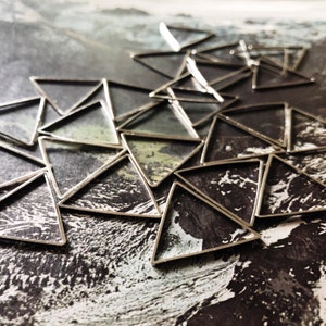 May include: A collection of silver metal triangle shapes arranged in a pattern on a black and white textured surface.