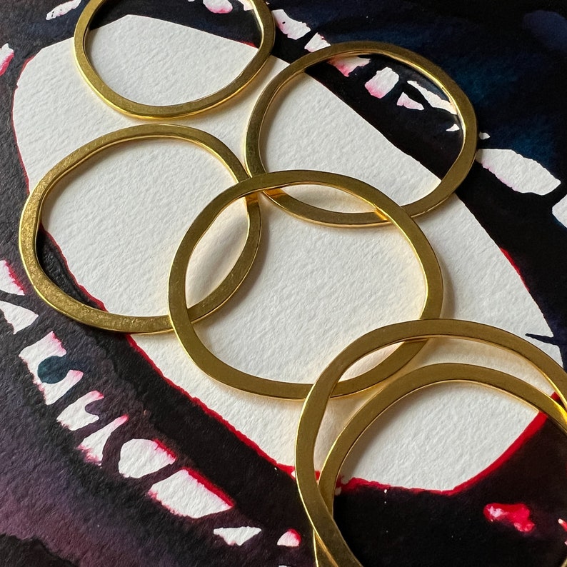 May include: Five gold-toned metal rings of varying sizes, stacked and overlapping, creating a circular pattern. The rings are arranged on a black and white background with red and white abstract patterns.