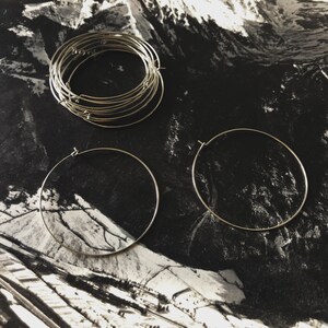 May include: Three silver hoop earrings, two large and one smaller, stacked on a black and white background.