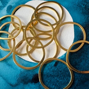 May include: A group of gold-colored metal rings, stacked and overlapping, on a blue and white background. The rings are all different sizes and shapes, and they create a visually interesting pattern.