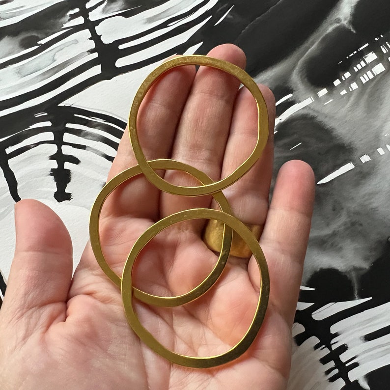 May include: Three gold-toned metal rings of different sizes, stacked on top of each other. The rings are smooth and have a polished finish.