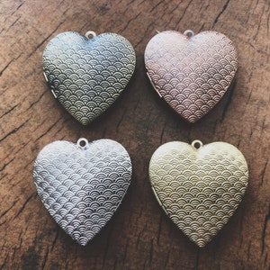 Op de afbeelding: Vier hartvormige hanger met een decoratief, golvend patroon. De hangers zijn zilver, goud, koper en een combinatie van zilver en goud.