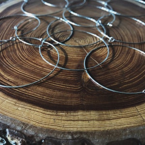 May include: A collection of silver-colored metal hoop earrings with clasps, scattered on a textured, brown wooden surface. The earrings are thin and circular, reflecting light. The wood grain is visible, creating a natural contrast.