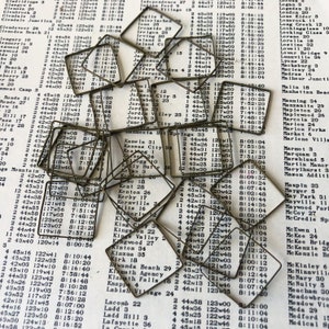 May include: A close-up of a collection of brass-colored metal squares with rounded corners. The squares are arranged in a random pattern on a white surface with black text. The squares are of varying sizes and are all the same color.