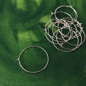 May include: A set of silver hoop earrings on a green background. The hoops are stacked on top of each other and are all the same size.