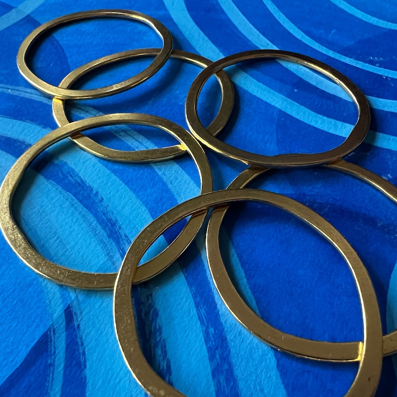 May include: Five gold-colored metal rings stacked on top of each other on a blue background with white brushstrokes.