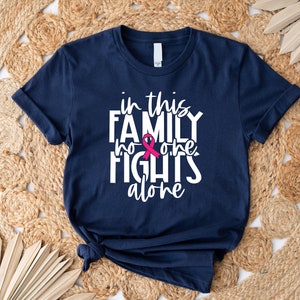 May include: A navy blue t-shirt with white text that reads "in this family no one fights alone". A pink ribbon is incorporated into the text.