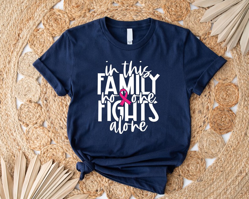 May include: A navy blue t-shirt with white text that reads "in this family no one fights alone". A pink ribbon is incorporated into the text.