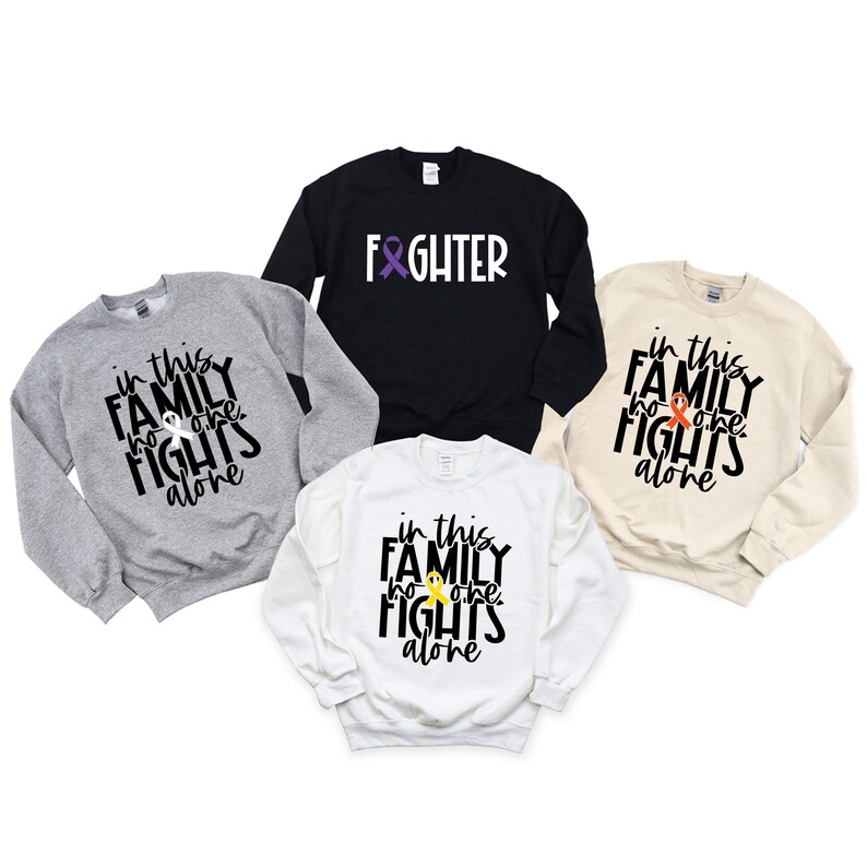 May include: Four sweatshirts with different colors and designs. The sweatshirts have the text "in this family no one fights alone" and a ribbon graphic. One sweatshirt is black with the text "fighter" and a ribbon graphic.