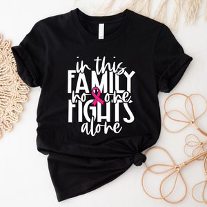 May include: Black t-shirt with white text that reads "in this family no one fights alone" with a pink ribbon graphic.