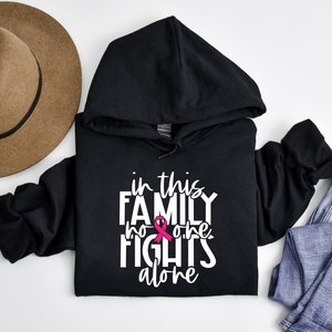 May include: Black hoodie with a white graphic that says "In this family no one fights alone" with a pink ribbon.