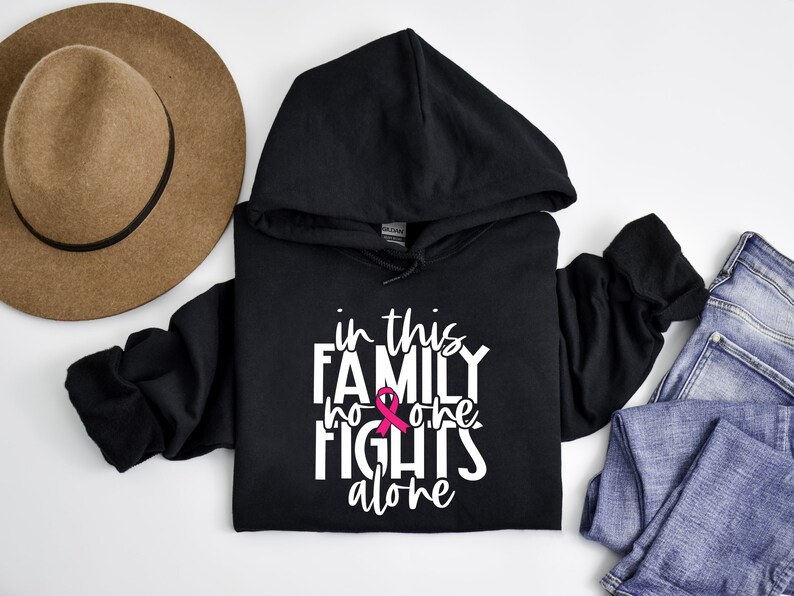 May include: Black hoodie with a white graphic that says "In this family no one fights alone" with a pink ribbon.