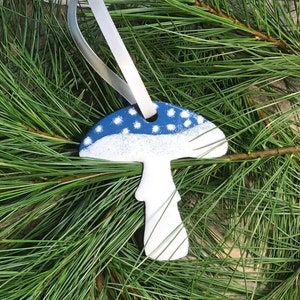 This mushroom ornament was designed using copper metal and vitreous enamel which is a powdered glass, fired in a kiln multiple times. It is available in white with blue accents and white with red accents!