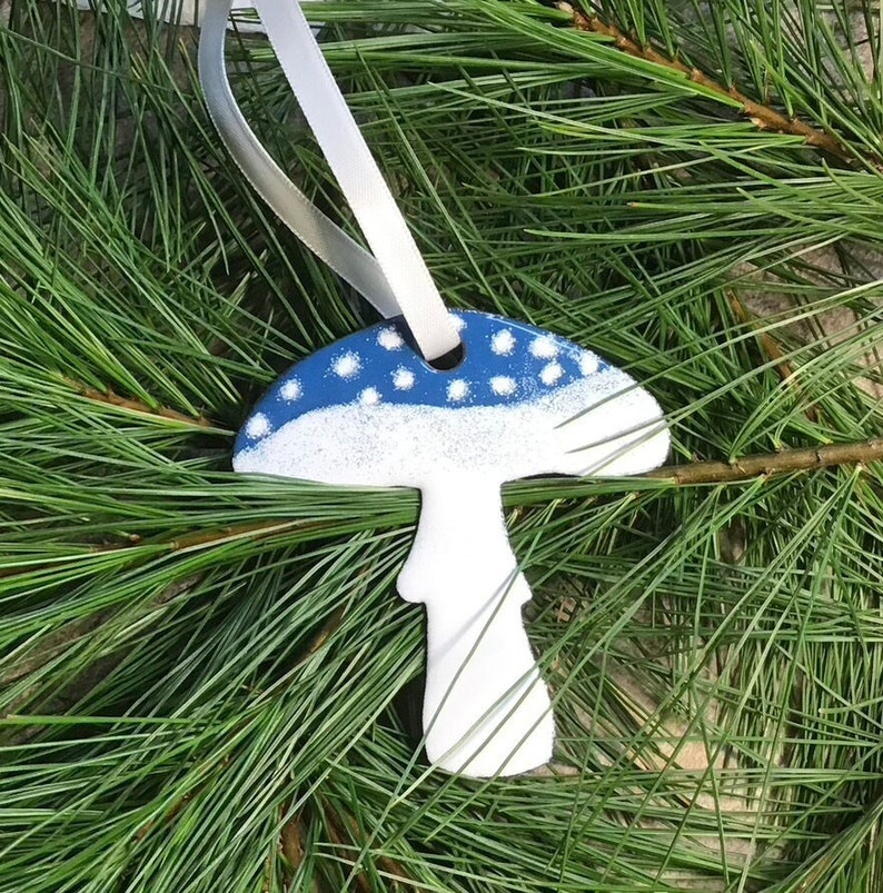 This mushroom ornament was designed using copper metal and vitreous enamel which is a powdered glass, fired in a kiln multiple times. It is available in white with blue accents and white with red accents!