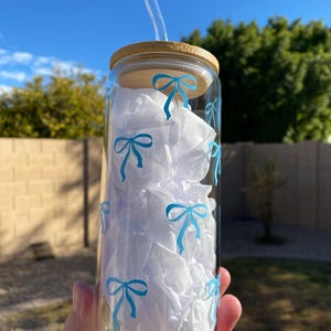May include: A clear glass water bottle with a bamboo lid and a blue bow pattern. The bottle has a glass straw.