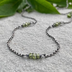 May include: A necklace featuring a dark oxidized silver chain with three distinct sections of light green faceted beads wrapped in thin silver wire. The chain links are small and round, creating a continuous loop with the wire-wrapped bead accents.