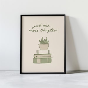 May include: A framed print with a beige background featuring the text "just one more chapter" in black cursive script. A green succulent plant in a beige pot sits atop a stack of three books.