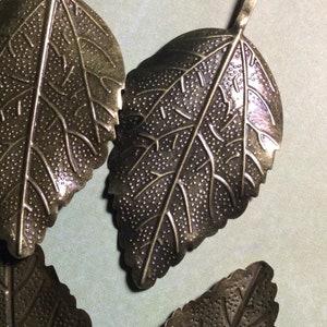 May include: Close-up of several bronze-colored leaf-shaped pendants. Each pendant has detailed veining and a textured surface. The leaves are arranged in a slightly overlapping pattern, showcasing their intricate design and metallic finish. Ideal for jewelry making.
