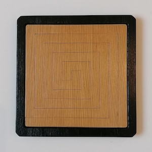 Peut inclure: Un puzzle carré en bois avec un cadre noir. Le puzzle présente un motif en spirale gravé dans le bois.