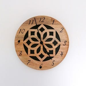 May include: A round wooden clock with black hands and black numbers. The clock face has a black geometric design.
