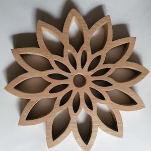 May include: A wooden, flower-shaped trivet with a natural finish. The trivet features a series of petal-shaped cutouts radiating from a central circular opening. The design is symmetrical and the wood grain is visible.