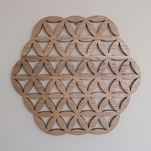 May include: A wooden wall hanging with a geometric design, featuring interlocking circles and triangular shapes. The natural wood has a light brown color and is mounted on a white wall. The design is symmetrical and decorative.