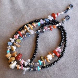 May include: A black beaded eyeglass chain with colorful gemstone beads. The chain features a variety of stones, including turquoise, red, pink, and brown.