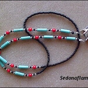 May include: A beaded chain featuring a long strand of small black beads accented with cylindrical turquoise beads, round red beads, and small silver-tone spacers. The chain terminates in two silver-tone metal clips. The text Sedonaflame is visible.