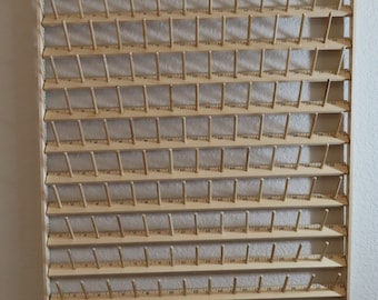 May include: A wooden thread rack with 20 rows of wooden pegs for holding spools of thread. The rack is mounted on a wall and has red plastic stoppers at the top.
