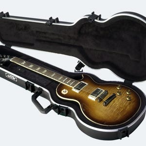 May include: A brown and black electric guitar in a black hard case with a silver trim. The case is open and the guitar is visible inside.