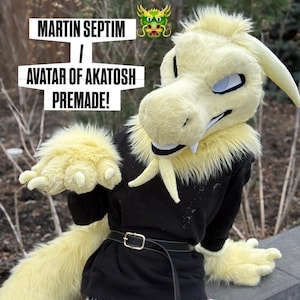 Può includere: Un costume da drago pre-fatto con testa, artigli e coda color crema. Il costume presenta un top nero e una cintura. Il testo sull'immagine recita "MARTIN SEPTIM / AVATAR OF AKATOSH PREMADE!"
