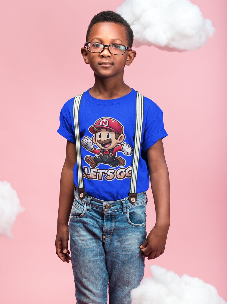 May include: A young person wearing a blue t-shirt with a cartoon character and the text "LET'S GO" printed on it. The shirt has white suspenders and the person is wearing blue jeans.