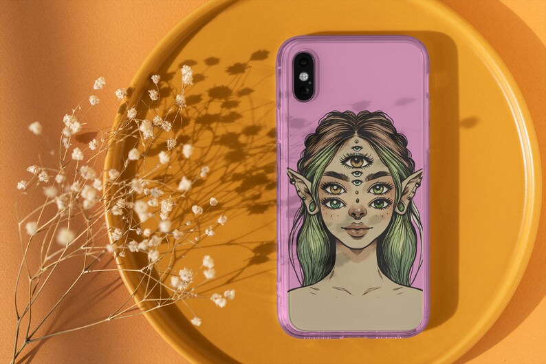 Op de afbeelding: Een roze telefoonhoesje met een afbeelding van een vrouw met meerdere ogen en elfenoren. De vrouw heeft groen haar en draagt een roze top.
