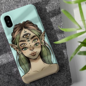Op de afbeelding: Een lichtblauwe telefoonhoes met een kleurrijke illustratie van een persoon met meerdere ogen en puntige oren. De persoon heeft groen haar en draagt een neusring.