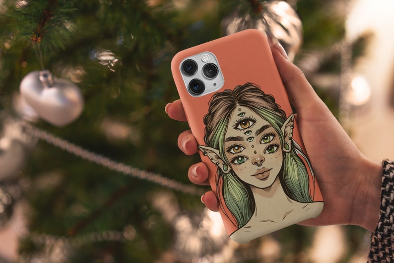 Op de afbeelding: Een koraalroze telefoonhoesje met een kleurrijke illustratie van een vrouw met meerdere ogen en elfenoren.
