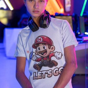 May include: A white t-shirt with a cartoon character wearing a red hat and overalls. The character is running and the text "LET'S GO" is printed below.