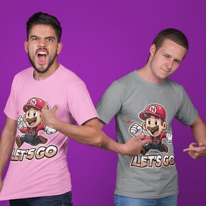 Puede incluir: Dos personas con camisetas con un personaje de dibujos animados corriendo y el texto "Let's Go". Una camiseta es rosa y la otra es gris.