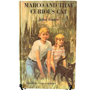 Puede incluir: Una portada de libro vintage titulada "Marco and That Curious Cat" de John Foster. La portada muestra a dos niños y un gato negro en un entorno herboso. Ilustrado por Lorence F. Bjorklund.