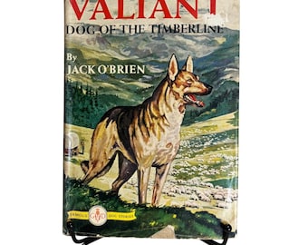 May include: Vintage book titled "Valiant Dog of the Timberline" by Jack O'Brien. The cover features a dog illustration in a mountain landscape with sheep. The book is displayed on a black metal stand.