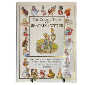 以下が含まれることがあります： 「The Classic Tales of Beatrix Potter」および「The Complete Adventures of Peter Rabbit and Friends」というタイトルのハードカバー本。白い表紙の中央には、庭にいるピーターラビットと、その周りを囲む様々な動物のキャラクターのイラストが描かれています。