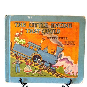 Könnte beinhalten: Vintage Kinderbuch mit dem Titel "The Little Engine That Could" von Watty Piper. Das Cover zeigt einen blauen Zug, einen Clown und Kinder. Das Buch ist ein Platt & Munk Classic, die vollständige Originalausgabe.
